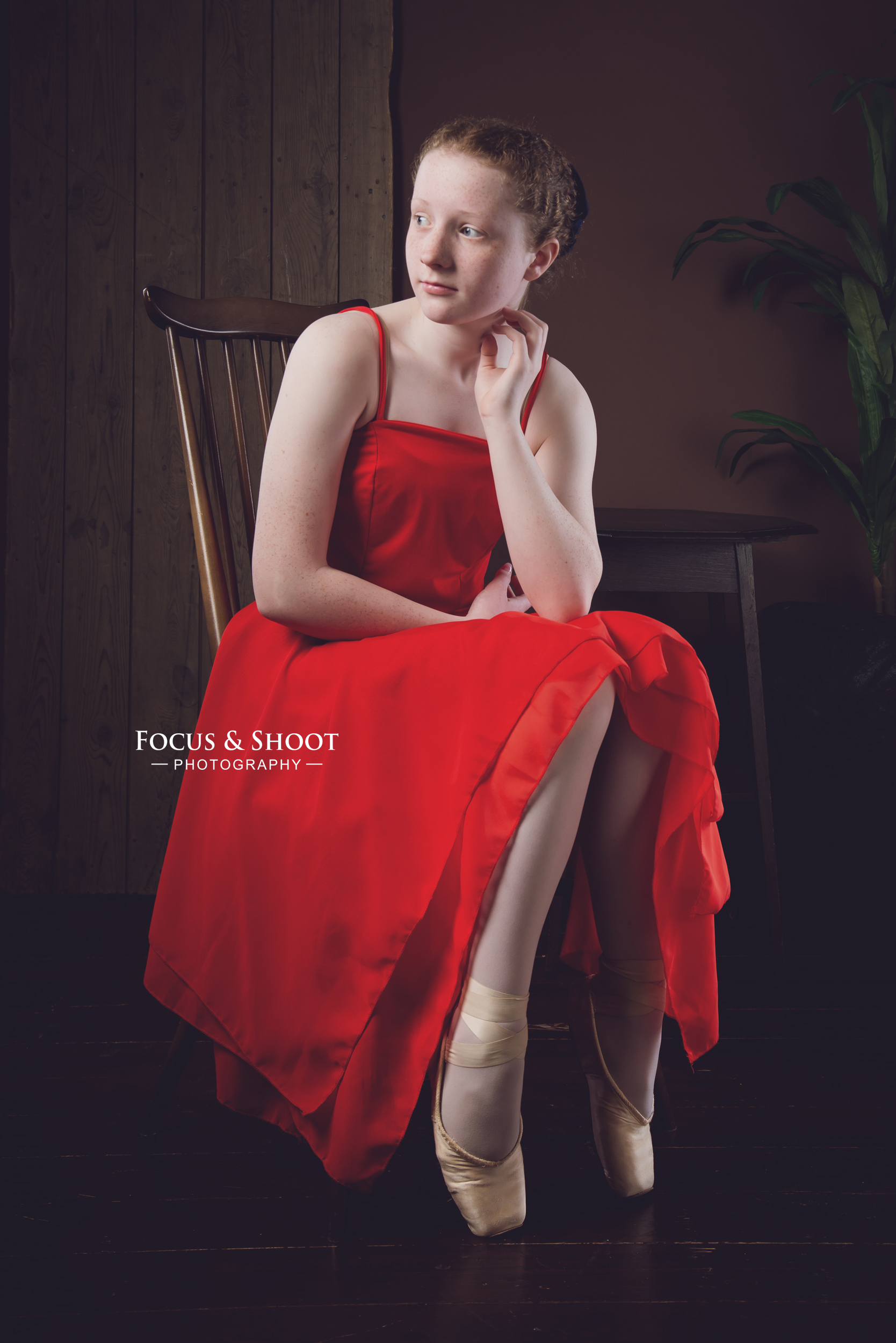 Young ballet dancer in a red dress, seated in pointe shoes
